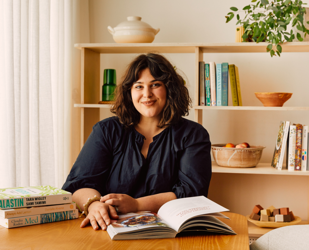 Julia Busuttil Nishimura sitting at a table with cookbooks. There is a bookcase in the background. 