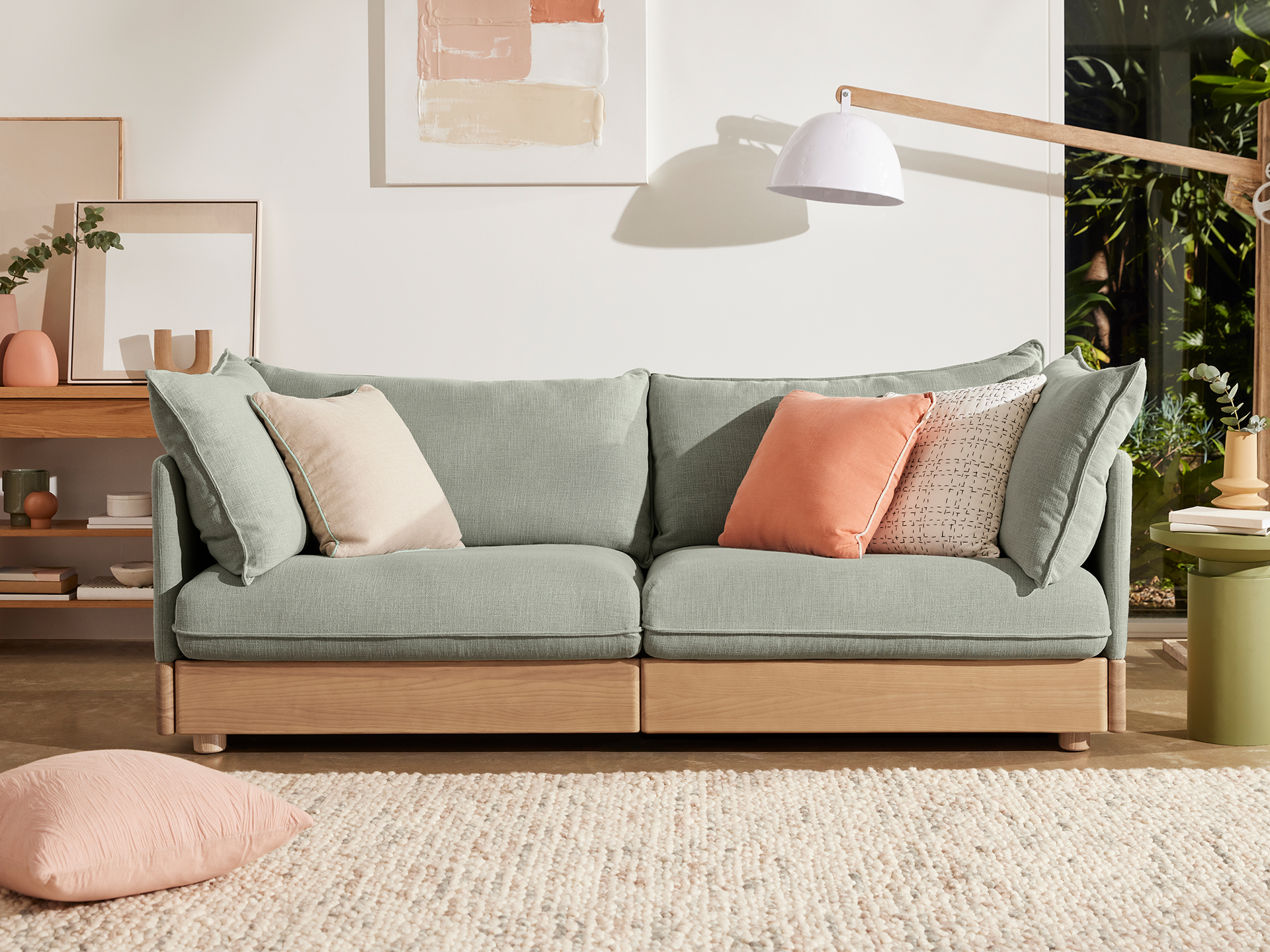 Three seater sofa with light green linen upholstery and timber storage shelves. 