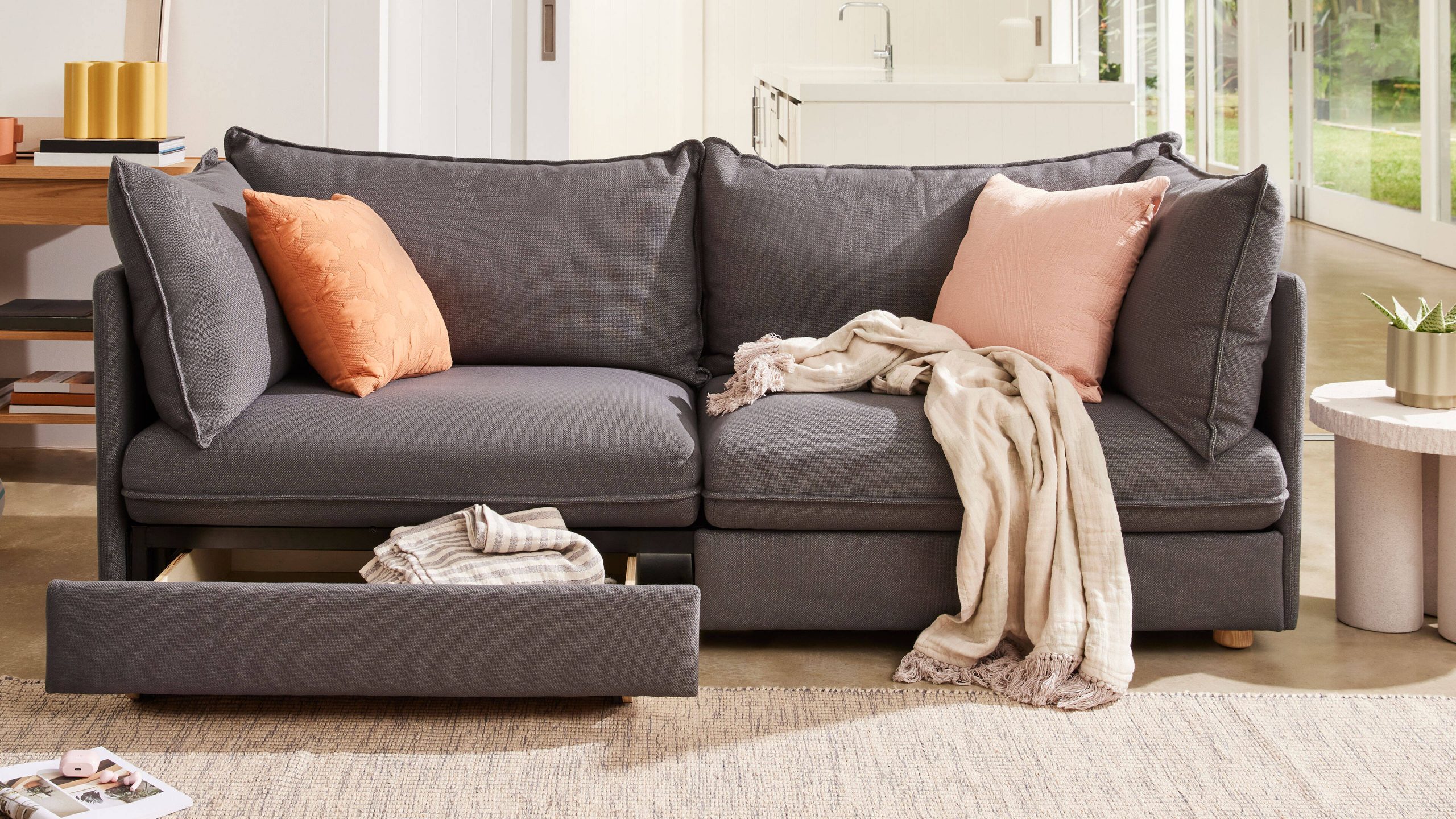 A grey three-seater, dark grey upholstered sofa with storage drawers.