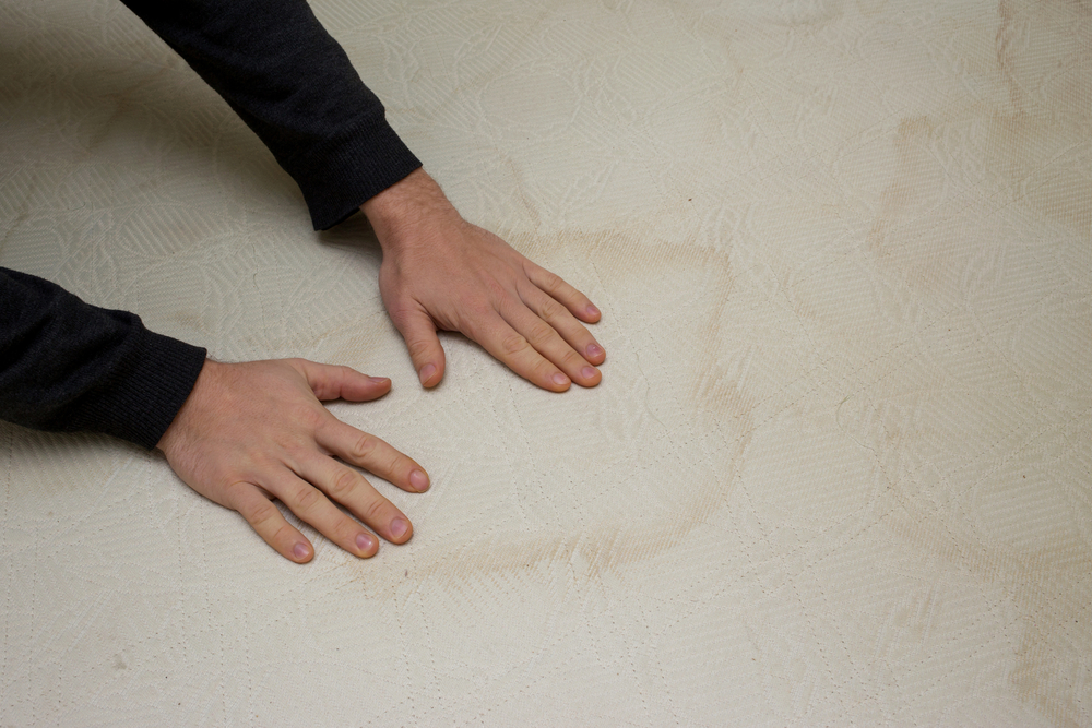 Two hands on a stained mattress with the person wondering how to clean the mattress