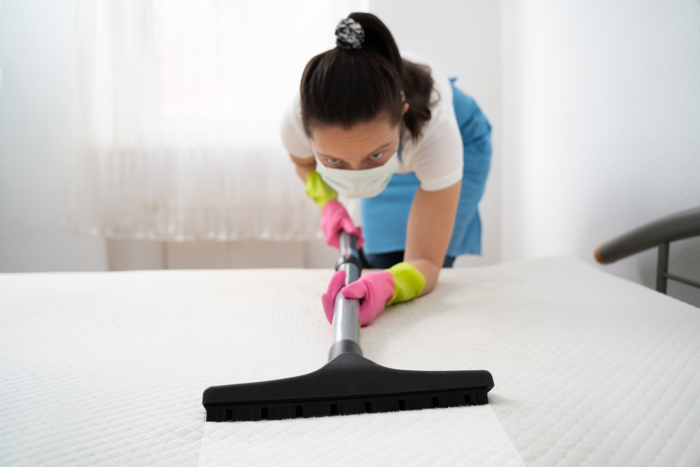 Female using a vacuum to get stains out of a mattress.