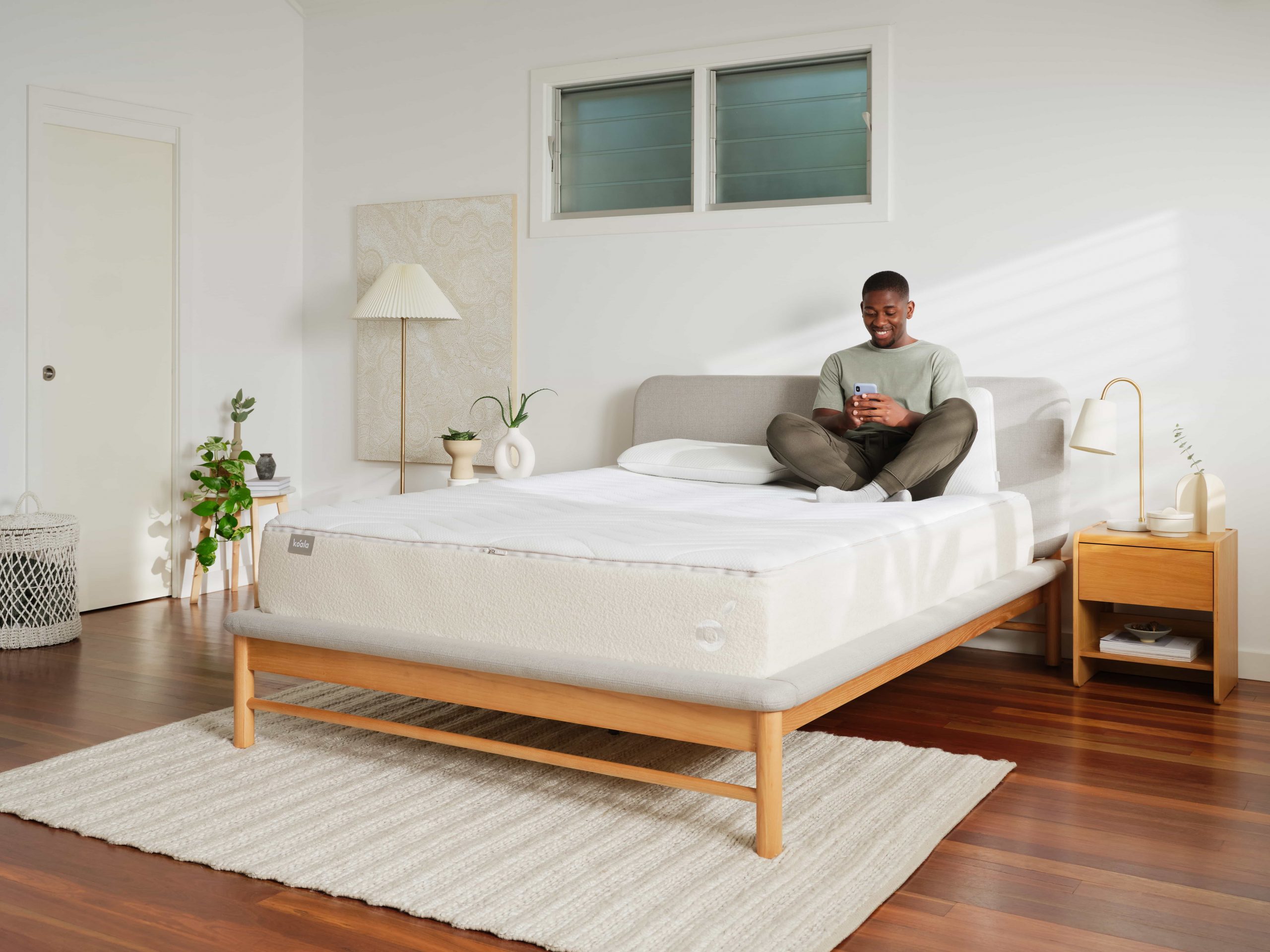  A man sits on a Koala mattress in a minimalist bedroom researching how often you should change your mattress on his smartphone.