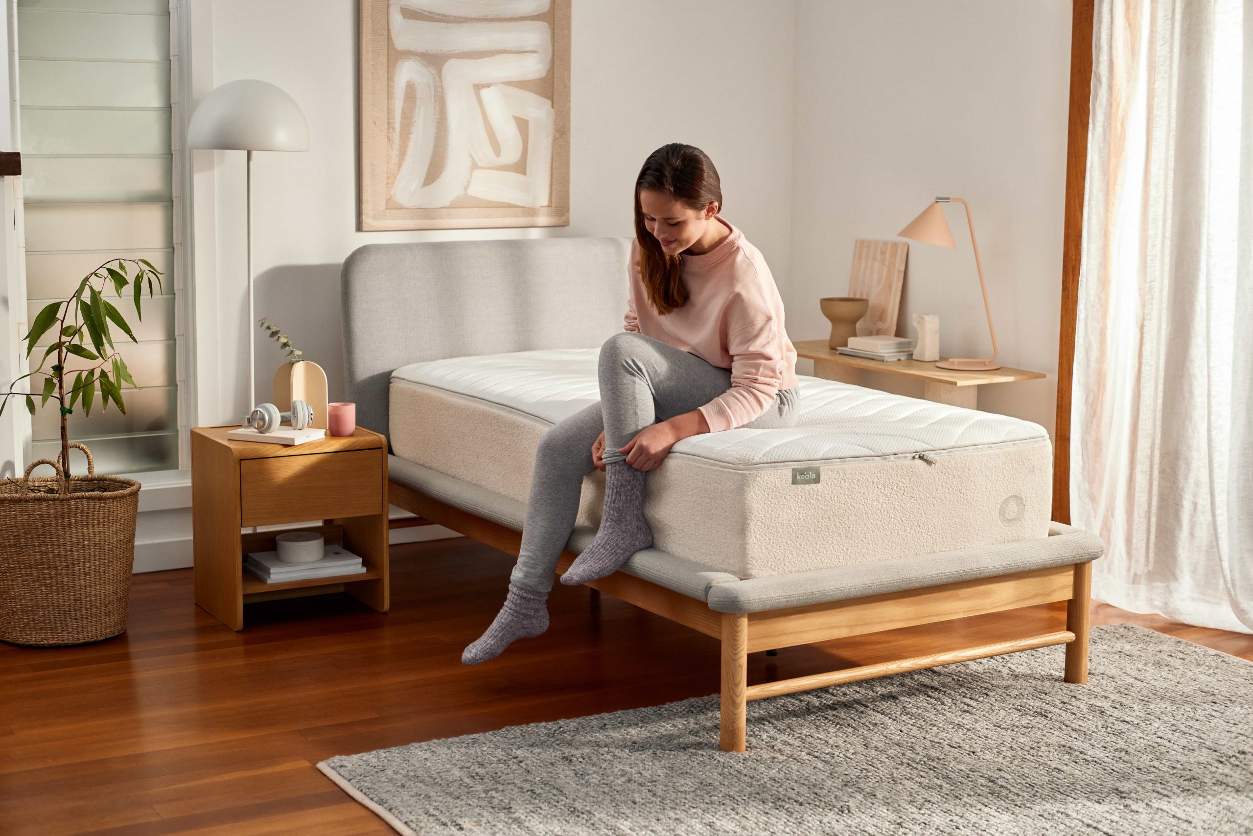 Woman with long brown hair sitting on a single mattress putting on her natural fibre pyjamas to be get to the ideal sleeping temperature