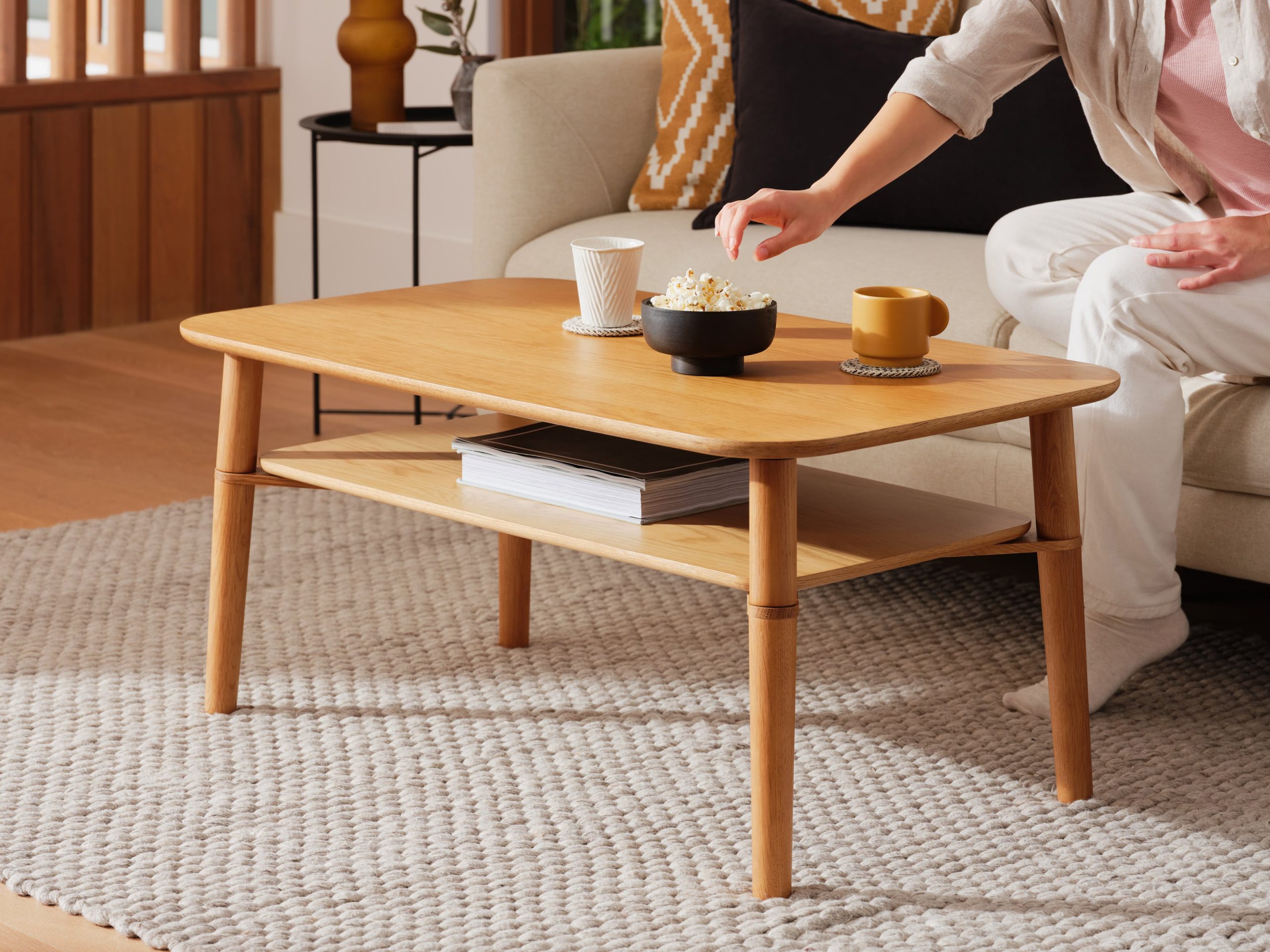 A woman reaches for a bowl of popcorn on her mid-century coffee table in a bright and clean living room