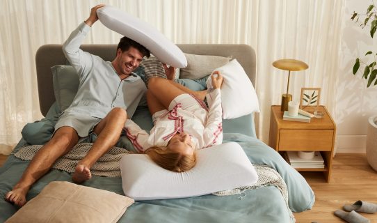 A playful couple laugh in bed after discovering the best pillow for side sleepers