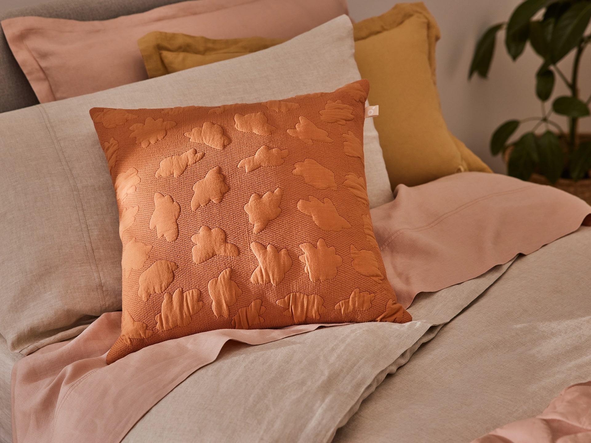 A mid-century modern bed featuring warm-toned bedding and a dark orange cushion from Koala