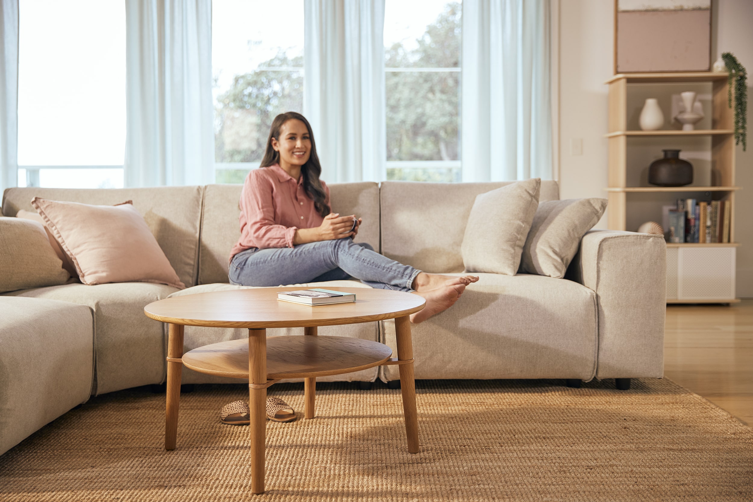 A smiling woman relaxes on her Koala sofa and behind her wood coffee table from Koala