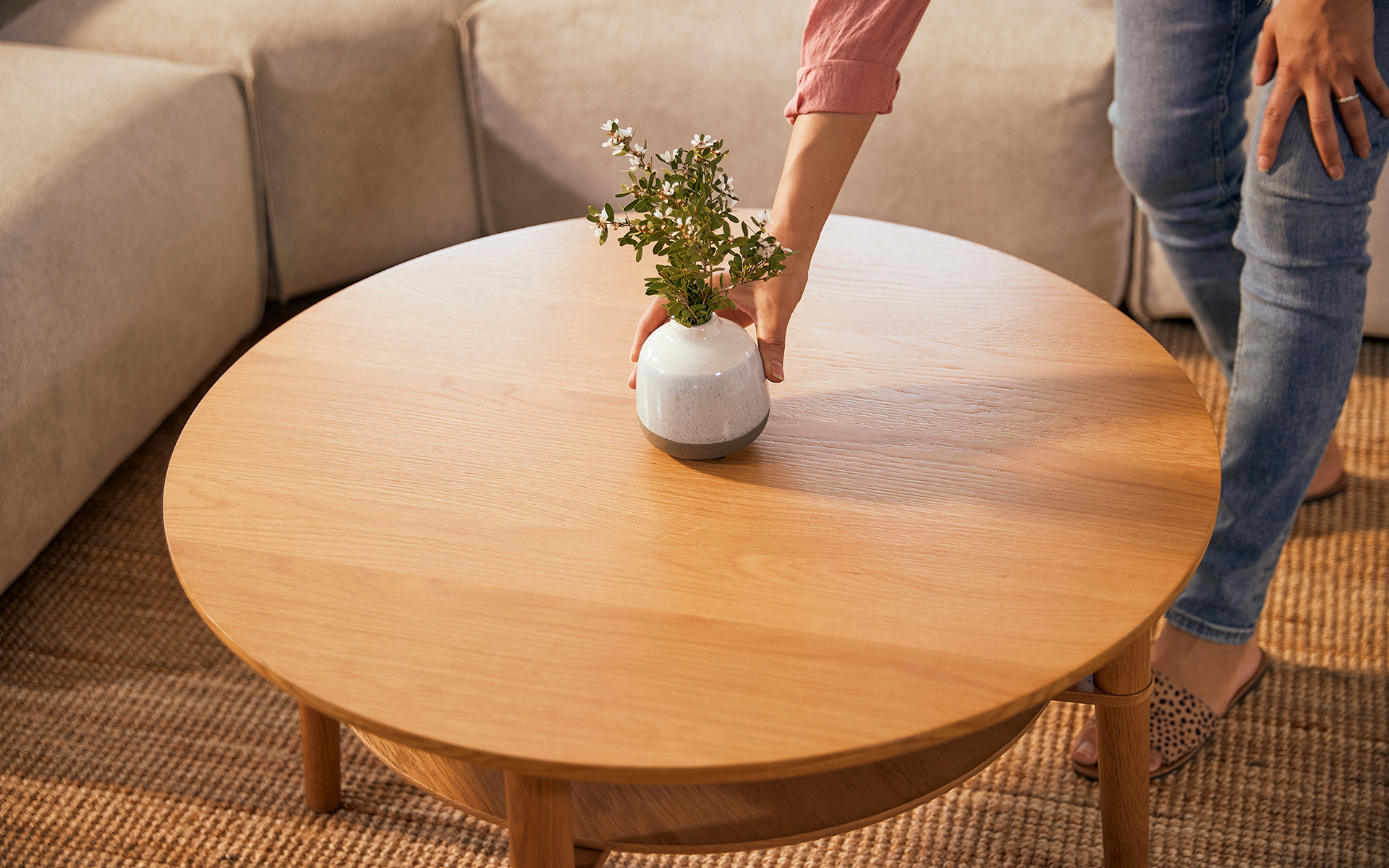 A woman starts decorating her coffee table with a simple vase of flowers