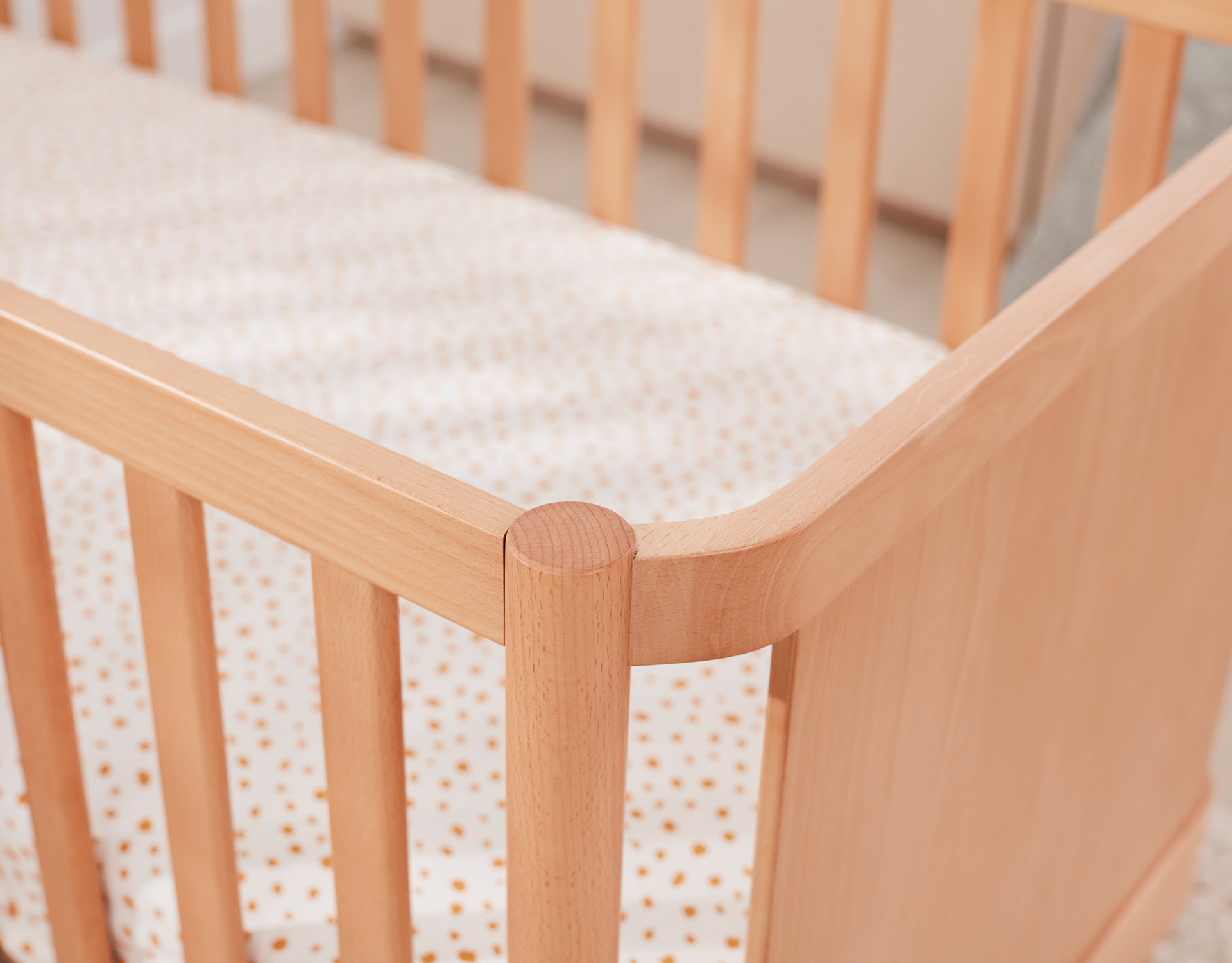 A close up shot of a light timber cot with best baby mattress inside , which is lightly patterned 