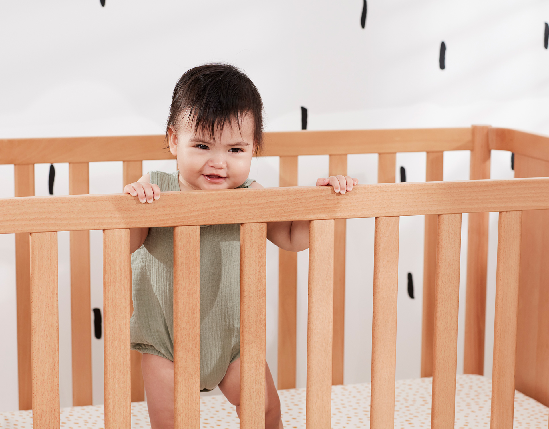 A baby stands up smiling in her cot, highlighting the importance of cot safety