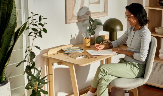 A smiling woman sits at her home office desk in her bright and clean home office workspace
