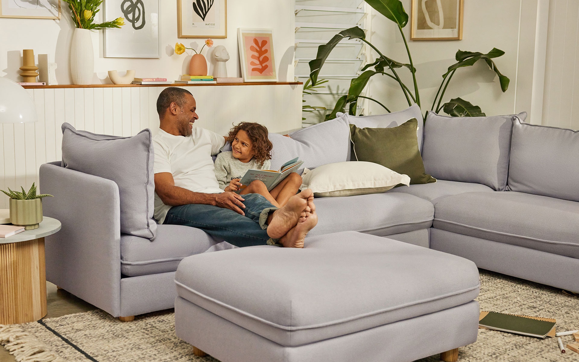 A father and child read a book and laugh on one of the best living room couches in Australia, the Koala Getaway sofa