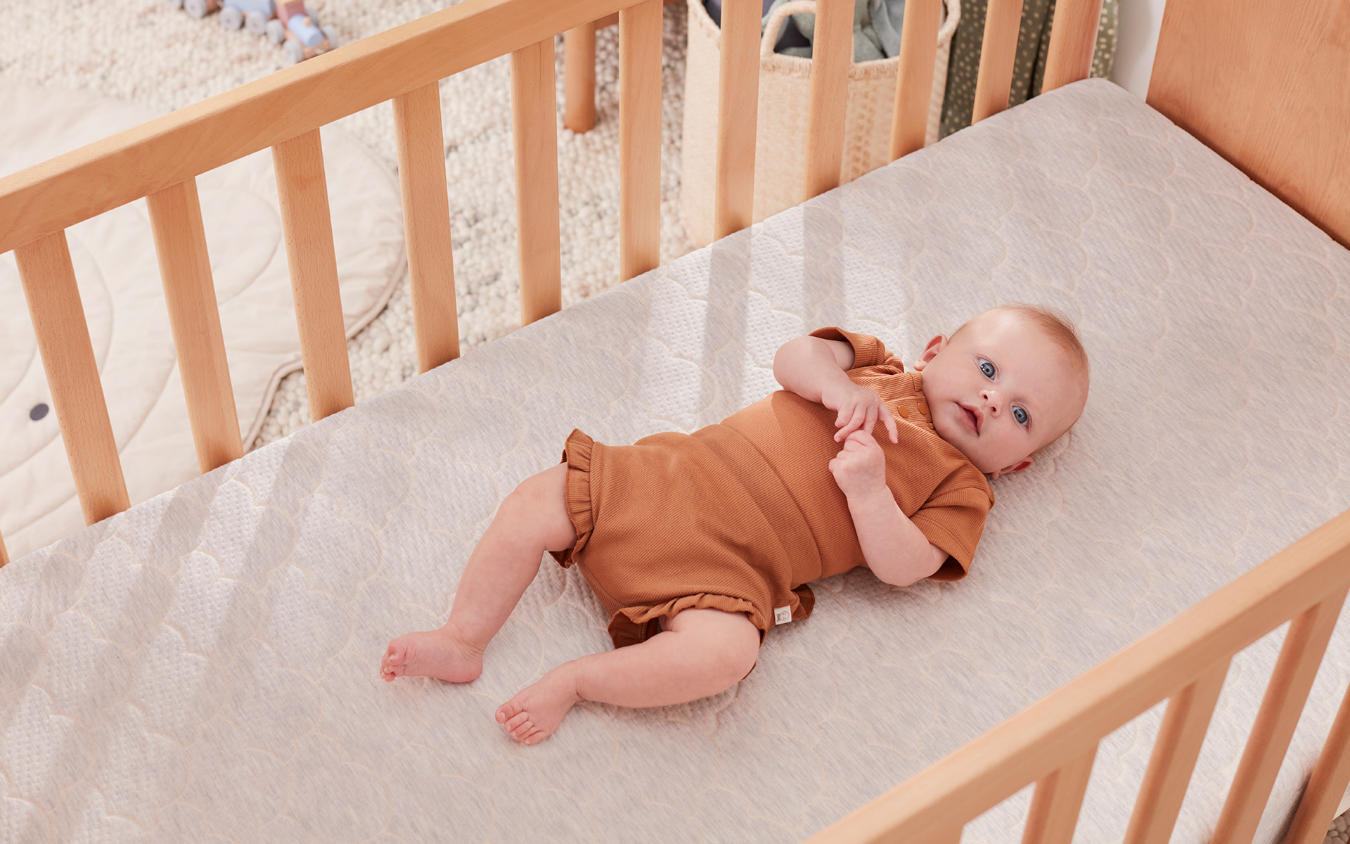 A baby lies on their back in a timber cot