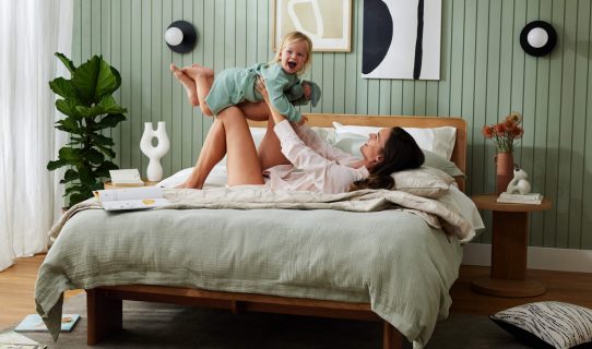A mother and child play on their bed in a pretty room with green feature wall and timber bedroom furniture