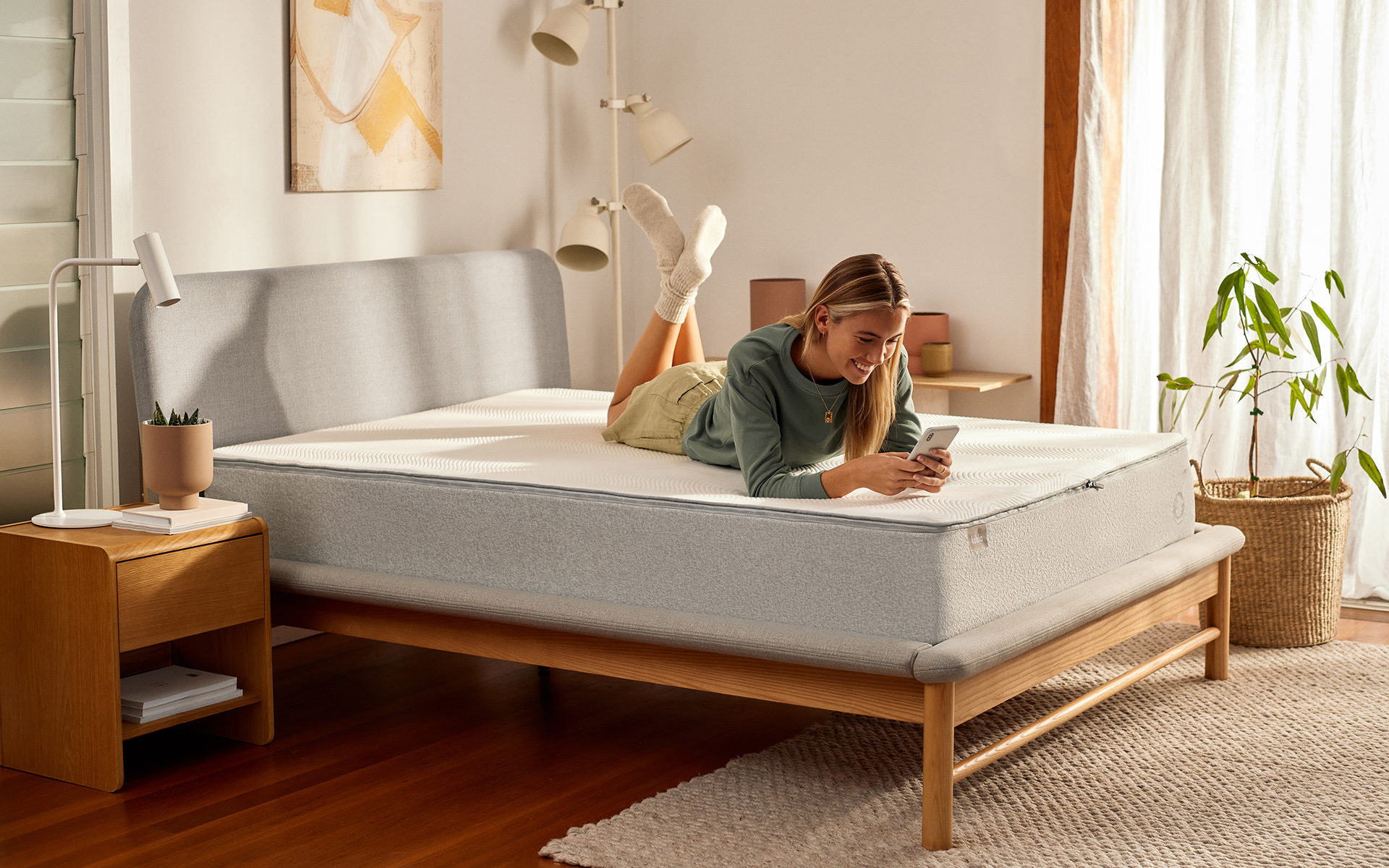 A woman lies on her Koala foam mattress and smiles down at her phone as she considers the advantages of a Koala mattress over a pocket springs mattress