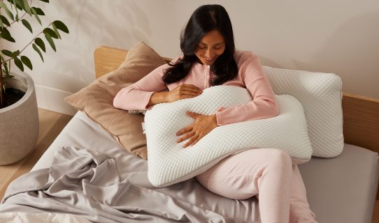 A woman snuggles up in bed after finding the best pillows Australia has to offer