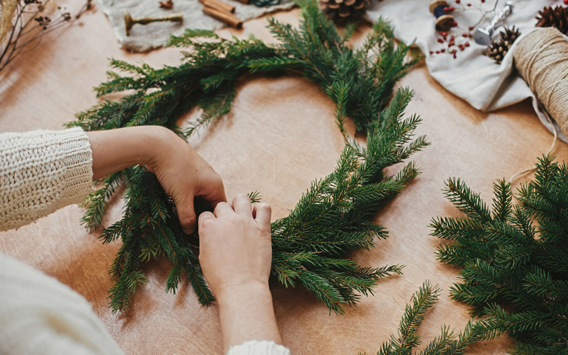 A woman creates a Christmas wreath from pine branches on a timber bench