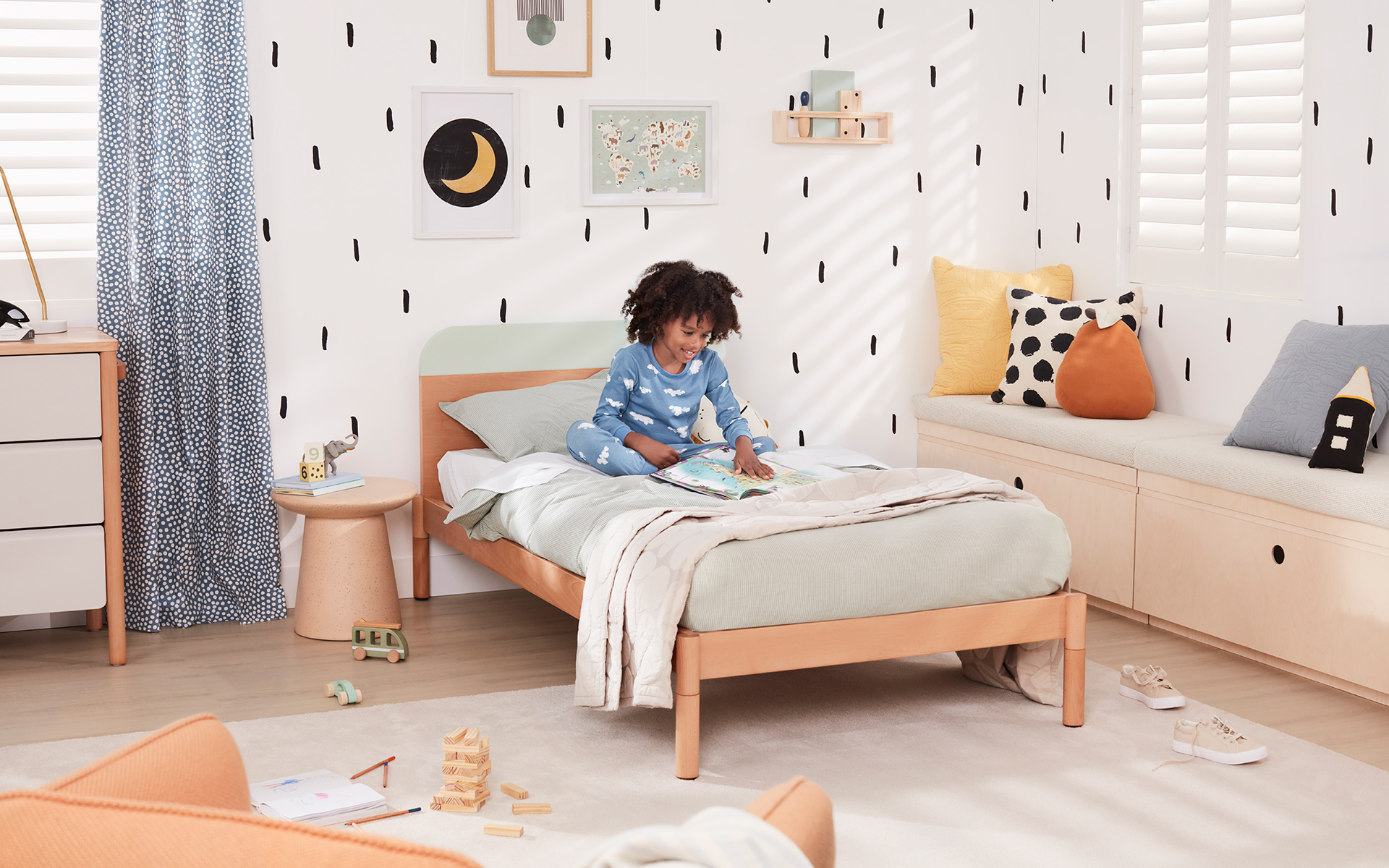 A young boy in his bright, fresh bedroom sits up in his toddler bed and smiles down at a book