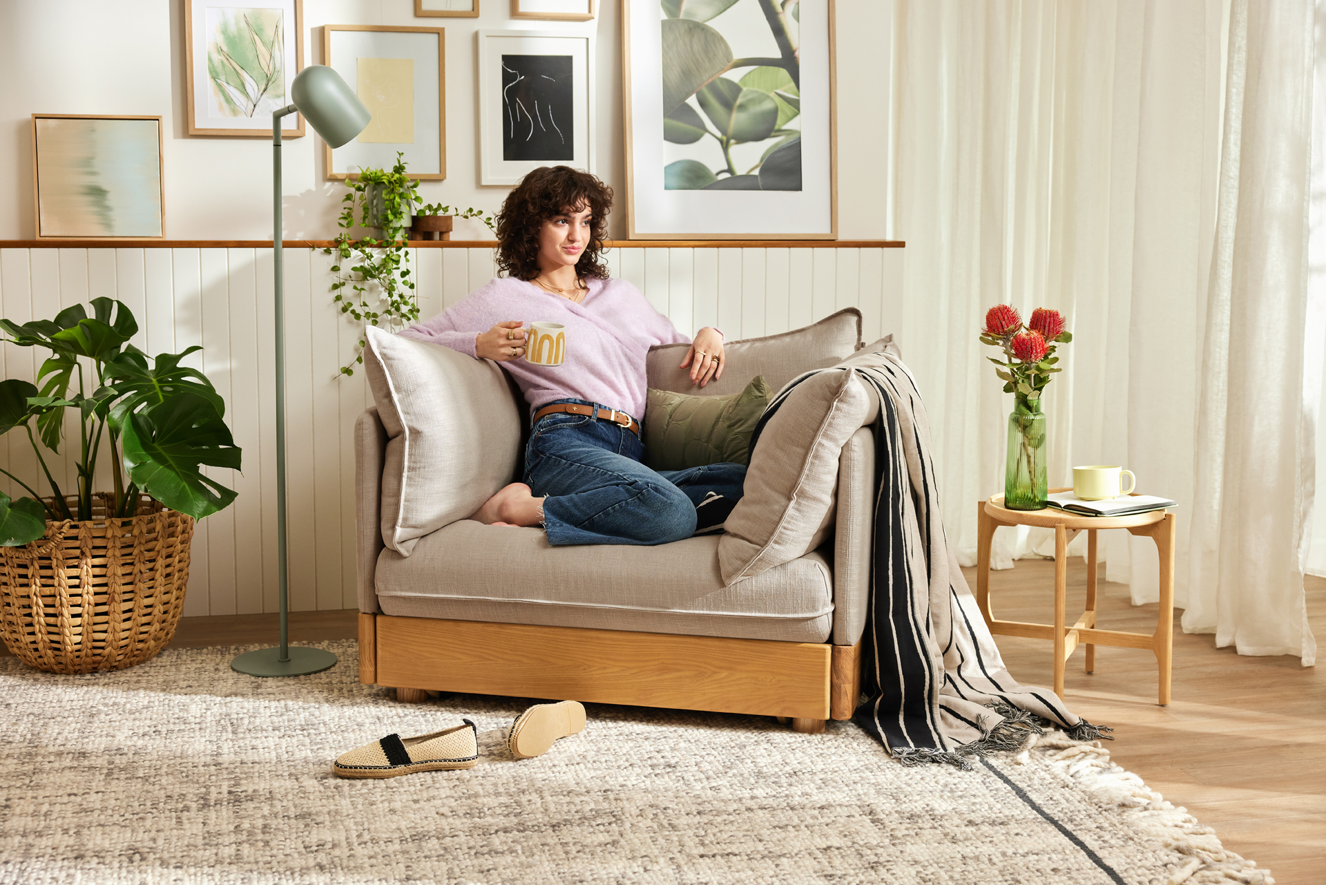 A woman relaxes on a Koala armchair in a living room with wall art, rug, plants and accessories