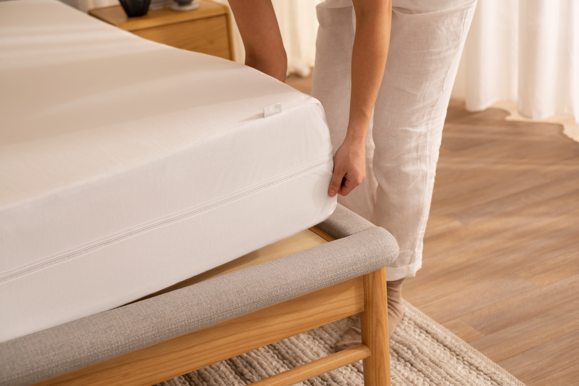 A close-up image of the corner of a bed as a woman finishes adjusting the mattress protector on the mattress