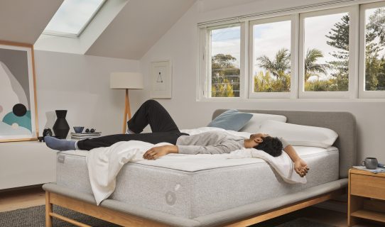 A man lies on a Koala mattress on a Koala bed frame in a bright, airy bedroom.