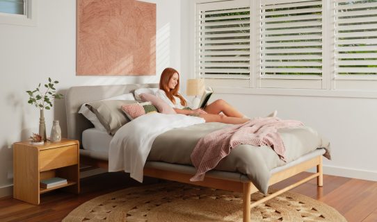 A woman reads a book on a Koala mattress and Koala Paddington Bed Base in a well-lit bedroom.