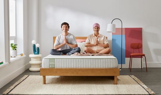A young, smiling couple relax in a meditation pose on their newly arrived Koala SE Mattress and Balmain bed base