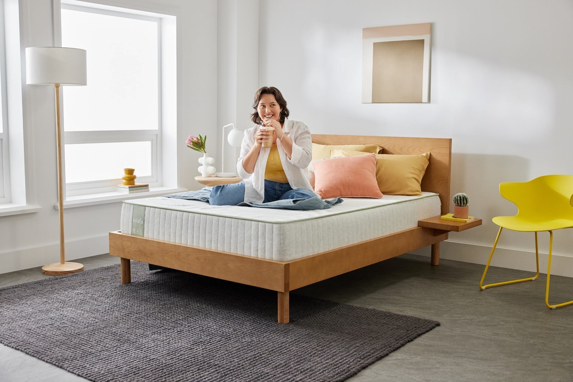 A young woman sits smiling after successfully setting up her new bedroom with Koala furniture and mattress