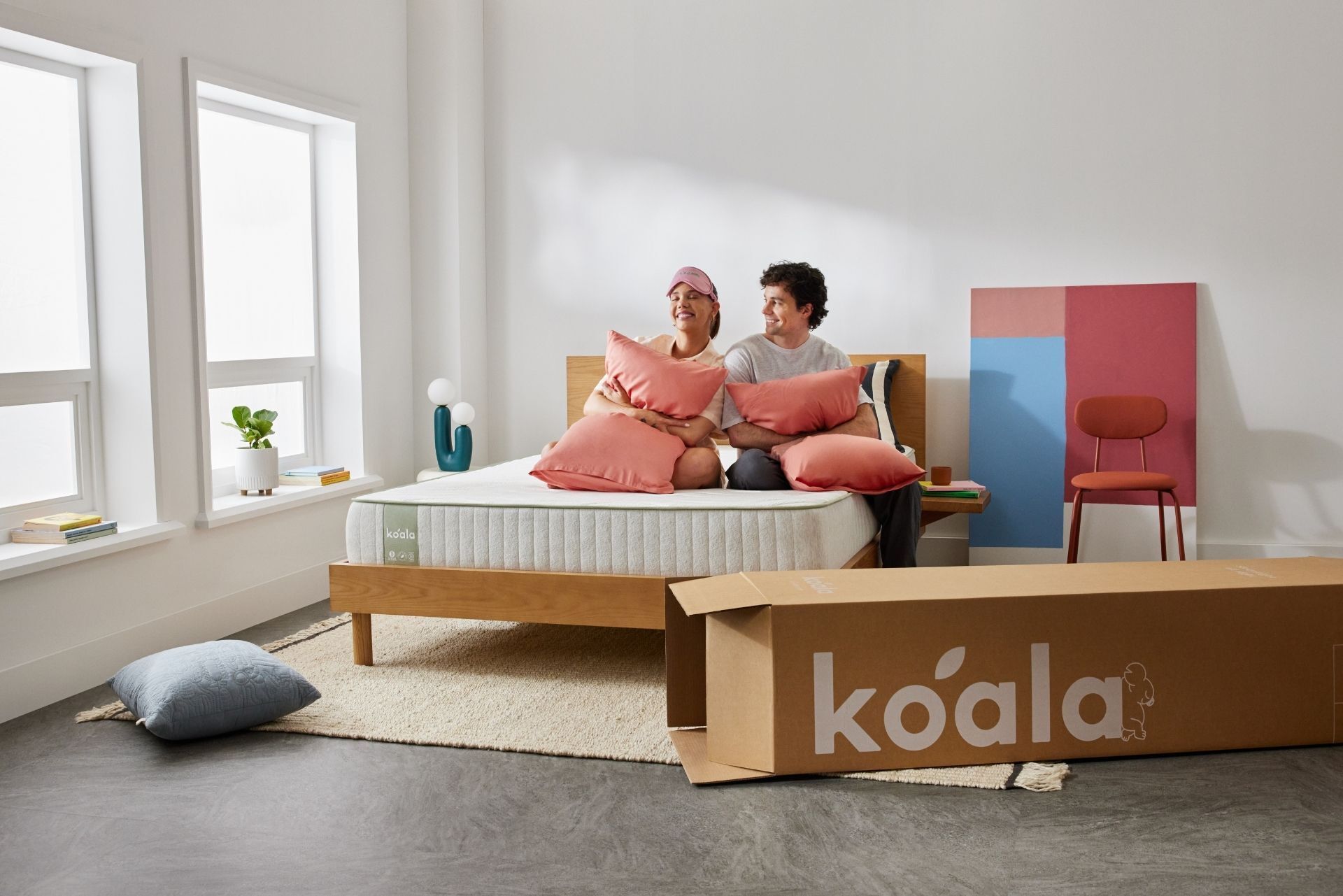 A couple sits on the Koala SE Mattress in their new house. The Koala bed box is featured in the image.