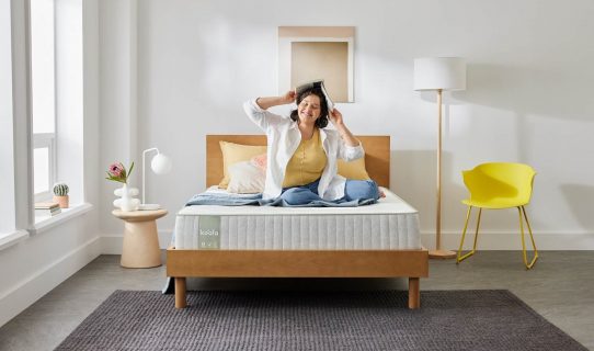 A woman sits happily on her Koala SE Mattress in a brightly lit room
