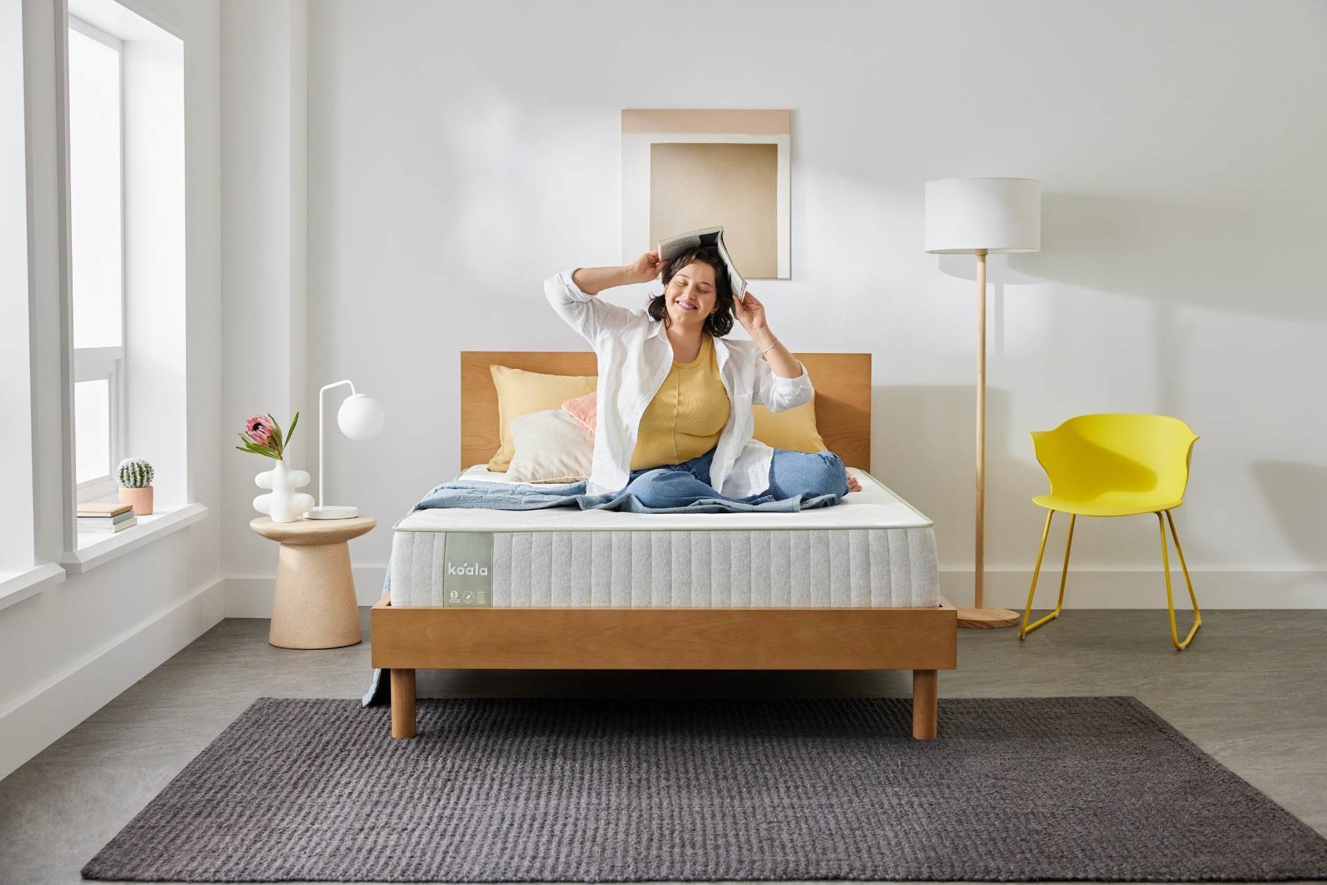 A woman sits happily on her Koala SE Mattress in a brightly lit room